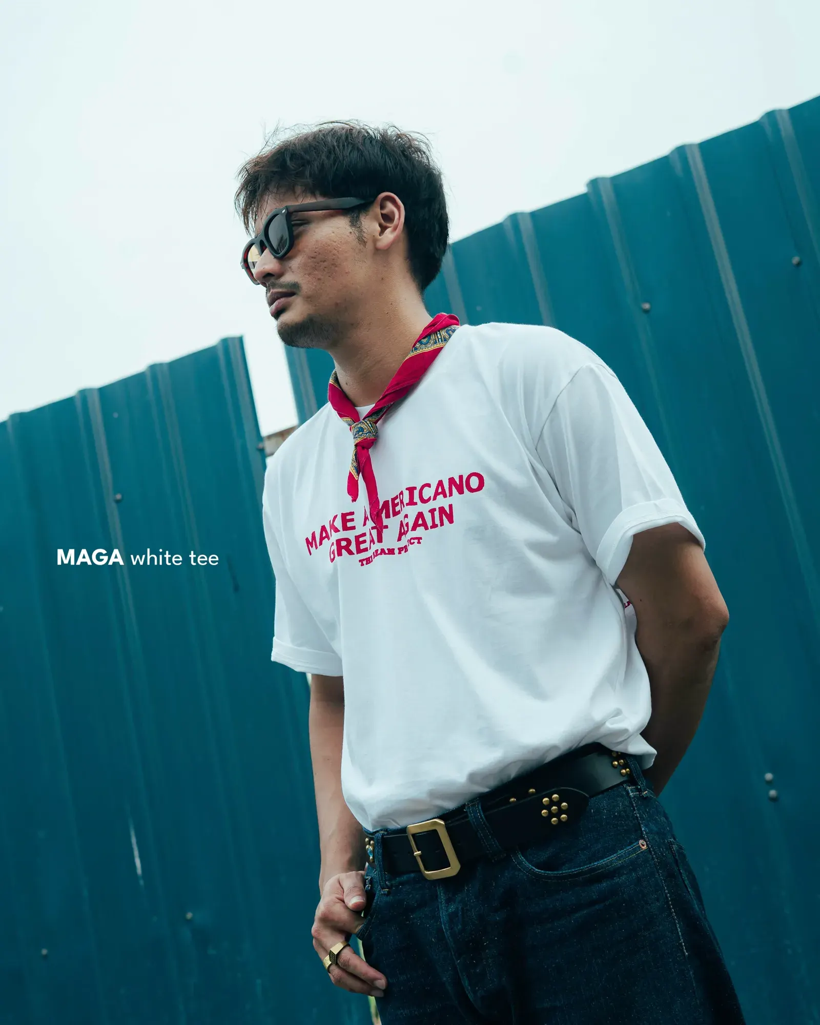 Model in the white MAGA tee and red bandana against a blue fence